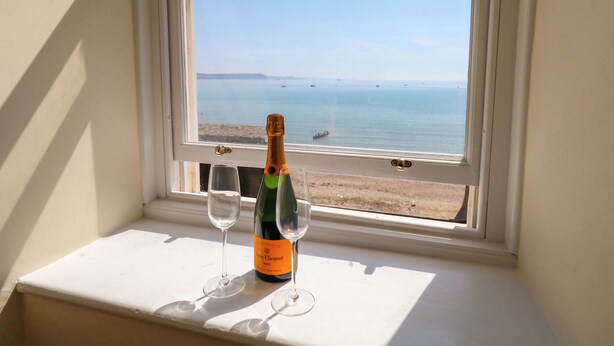 Een fles champagne en twee glazen op een vensterbank, met uitzicht op de zee.