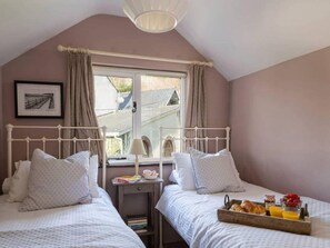 Ein Schlafzimmer mit zwei Betten, einem Fenster mit Vorhängen, einem Nachttisch mit Büchern und einem Tablett mit Frühstück.