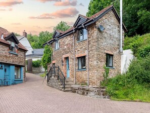 Ein Steinhaus mit einer Treppe, die zum Eingang führt, umgeben von Grünpflanzen.