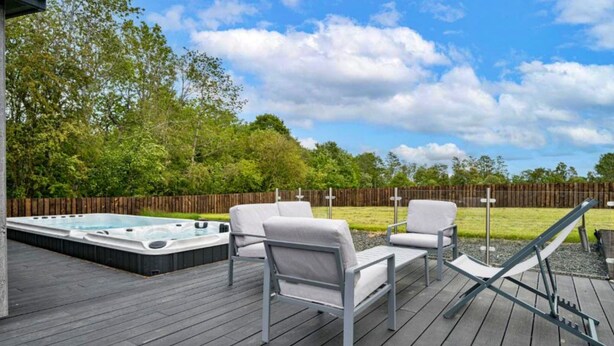 Una terraza con mobiliario exterior, un jacuzzi y una valla de madera.