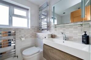 A modern bathroom with a toilet, sink, and mirror. - Countryside Escape Near Hergest Ridge (Kington)
