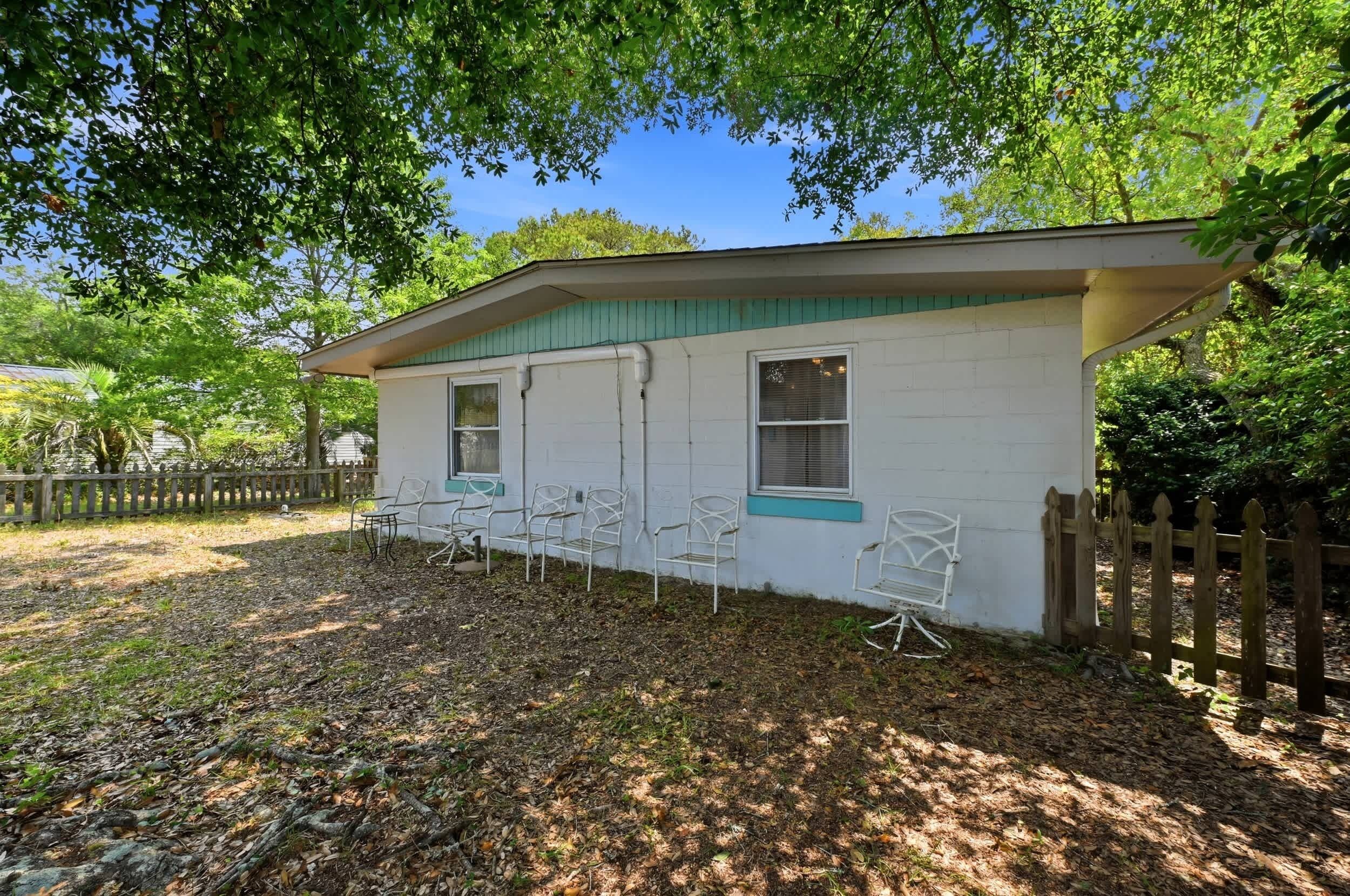 A small, single-story building with a porch area, white exterior walls, and a green roof. There are several white metal chairs arranged on the porch.