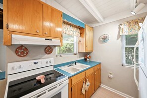 A kitchen with wooden cabinets, a stove, a sink, and a clock on the wall. - Seabright Surf Shack | Oak Island Beach Bungalow by Brunswick Vacation Rentals (Oak Island)
