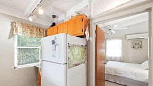 A compact room with a bed, a refrigerator, and a window with blinds. - Seabright Surf Shack | Oak Island Beach Bungalow by Brunswick Vacation Rentals (Oak Island)