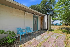 A house with a garage, a porch with two chairs, and a wooden fence. - Seabright Surf Shack | Oak Island Beach Bungalow by Brunswick Vacation Rentals (Oak Island)