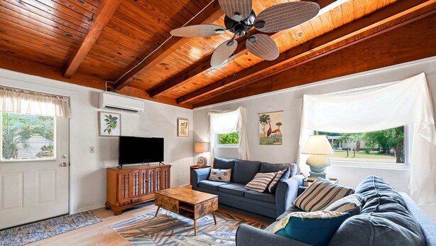 A living room with a wooden ceiling, a television, a sofa, a coffee table, and a patterned rug. - Seabright Surf Shack | Oak Island Beach Bungalow by Brunswick Vacation Rentals (Oak Island)