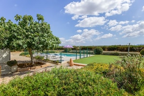Zona de piscina con un deck cercado, césped y un árbol.