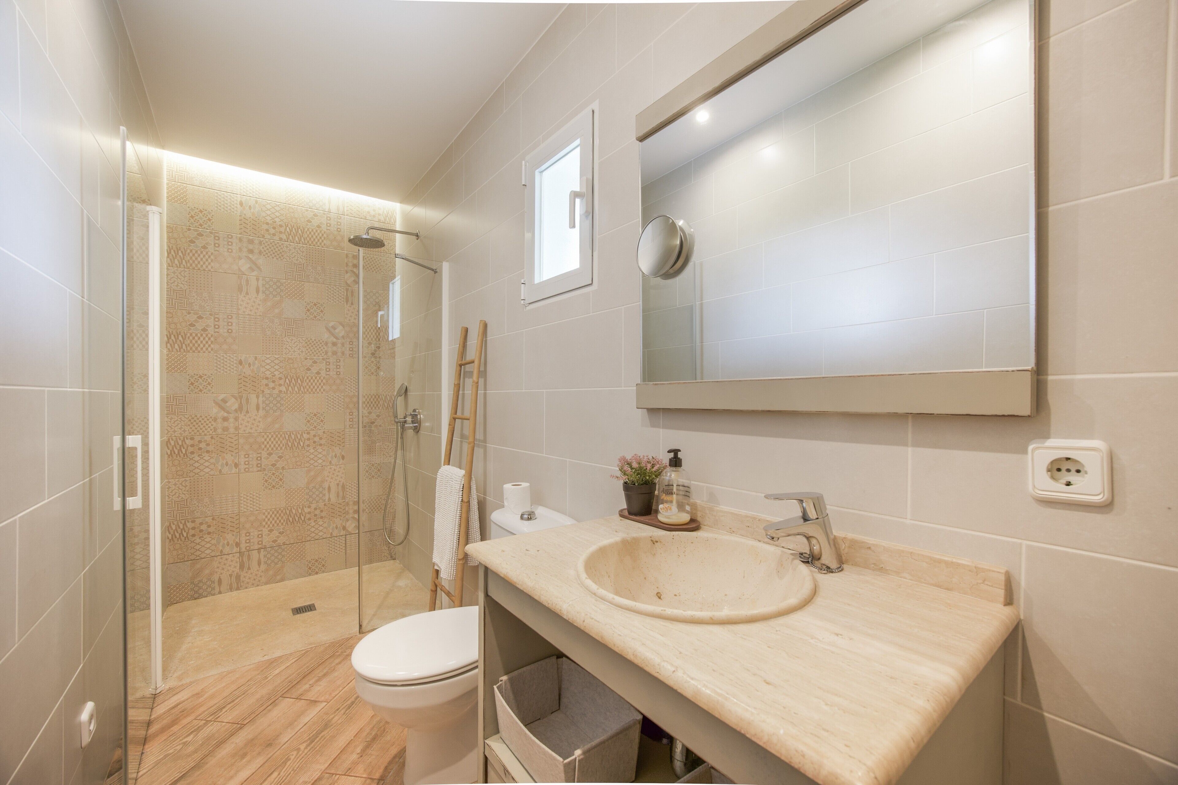 A modern bathroom with a glass shower enclosure, a toilet, a sink with a mirror above it, and a potted plant on the sink.