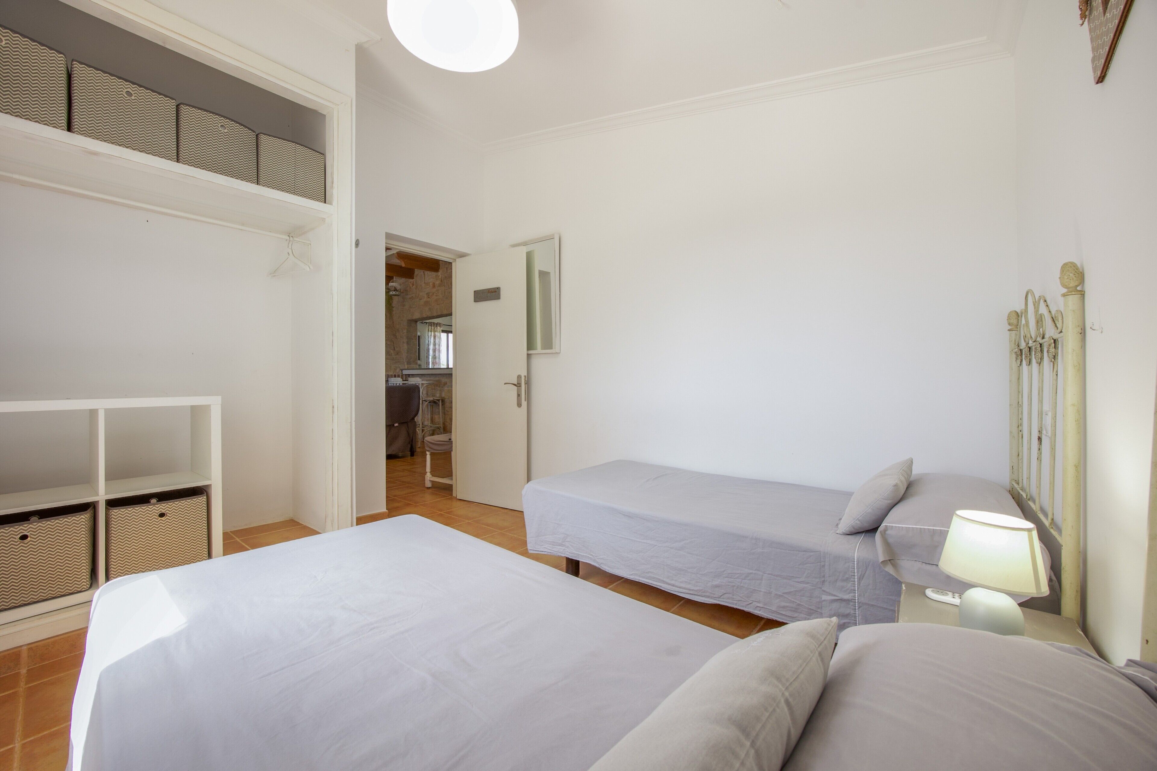Un dormitorio con dos camas individuales, una mesita de noche con lámpara, un armario y un baño que se ve a través de una puerta abierta.