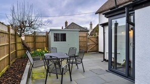 A patio area with a table and chairs, a small shed, and a wooden fence. - Nice Cottage in High Bickington (Umberleigh)