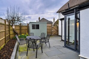 Ein Patio mit Tisch und Stühlen, eine kleine Gartenhütte und ein Holzzaun.