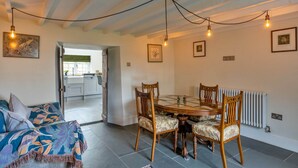 A dining area with a round table, four chairs, and a ceiling with exposed beams and hanging light bulbs. - Nice Cottage in High Bickington (Umberleigh)