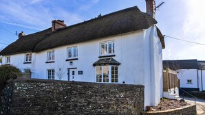 A traditional white building with a thatched roof, a stone wall in front, and a sign indicating it is a cottage. - Nice Cottage in High Bickington (Umberleigh)