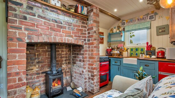 A cozy kitchen with a brick fireplace, red appliances, and a blue cabinet. - Rustic Romantic Cottage in Llangadog (Llangadog)