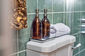Ein Badezimmer mit Toilette, zwei Seifenspendern, einem Handtuch und einem dekorativen, goldgerahmten Spiegel.