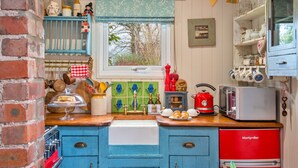 A kitchen with blue cabinets, a red refrigerator, and a window with a view of trees. - Rustic Romantic Cottage in Llangadog (Llangadog)