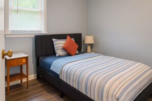 Ein Schlafzimmer mit einem Bett, einem Nachttisch, einer Lampe und einem Fenster mit Jalousien.