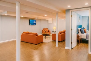 A modern living room with orange sofas, a coffee table, and a TV mounted on the wall. - Executive 4BR Home Fully Furnished. CALL IT HOME 30+Day (Louisville)