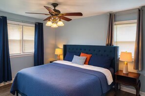 A hotel room with a bed, a ceiling fan, two bedside lamps, and a window with curtains. - Executive 4BR Home Fully Furnished. CALL IT HOME 30+Day (Louisville)