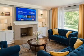 A living room with a fireplace, a television mounted above it, and a large window with curtains. - Executive 4BR Home Fully Furnished. CALL IT HOME 30+Day (Louisville)