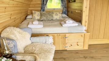Ein gemütliches Blockhauszimmer mit Bett, Stuhl, kleinem Tisch und Fenster.