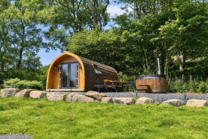 Una cabaña de madera con techo curvo, un patio con mobiliario exterior y un jacuzzi.