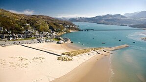 A coastal area with a sandy beach, a pier extending into calm waters, and a hillside with buildings. - Cesailgwm Glamping Snowdonia (Dolgellau)