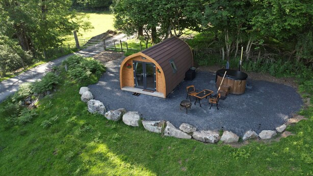 A small wooden cabin with a curved roof, a hot tub, and outdoor seating. - Cesailgwm Glamping Snowdonia (Dolgellau)
