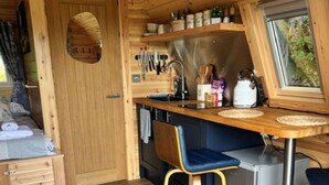 A compact kitchen with wooden cabinetry, a sink, and bar stools. - Cesailgwm Glamping Snowdonia (Dolgellau)