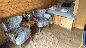 A cozy cabin interior with a bed, two upholstered chairs, a woven rug, and a small table with a vase of flowers. - Cesailgwm Glamping Snowdonia (Dolgellau)