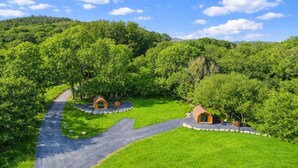 A lush green landscape with two small, dome-shaped structures surrounded by trees, connected by a winding path. - Cesailgwm Glamping Snowdonia (Dolgellau)