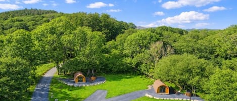 A lush green landscape with two small, dome-shaped structures surrounded by trees, connected by a winding path.