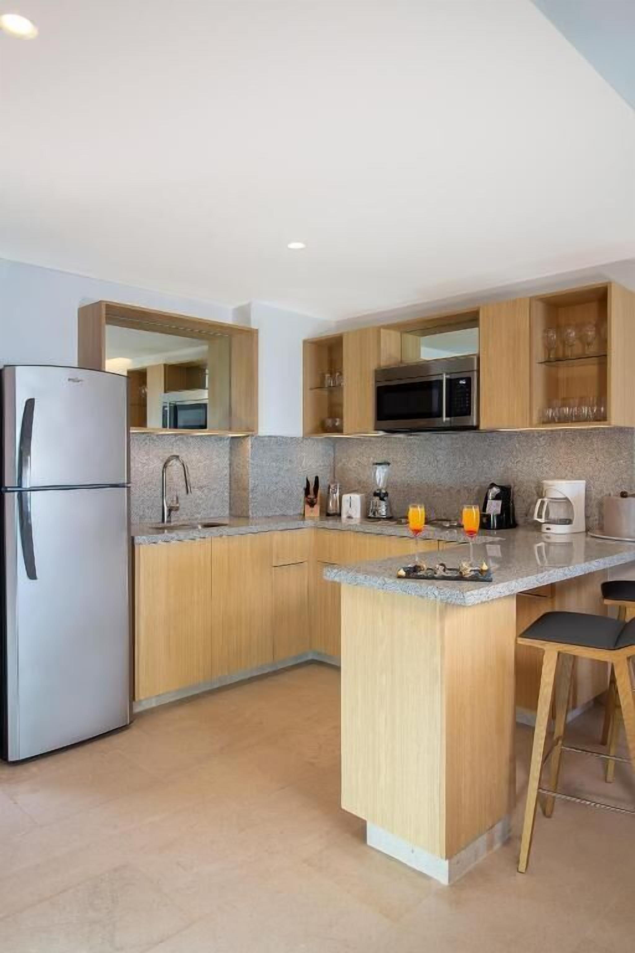 Cocina moderna con alacenas de madera, refrigerador de acero inoxidable, microondas y una barra con taburetes.