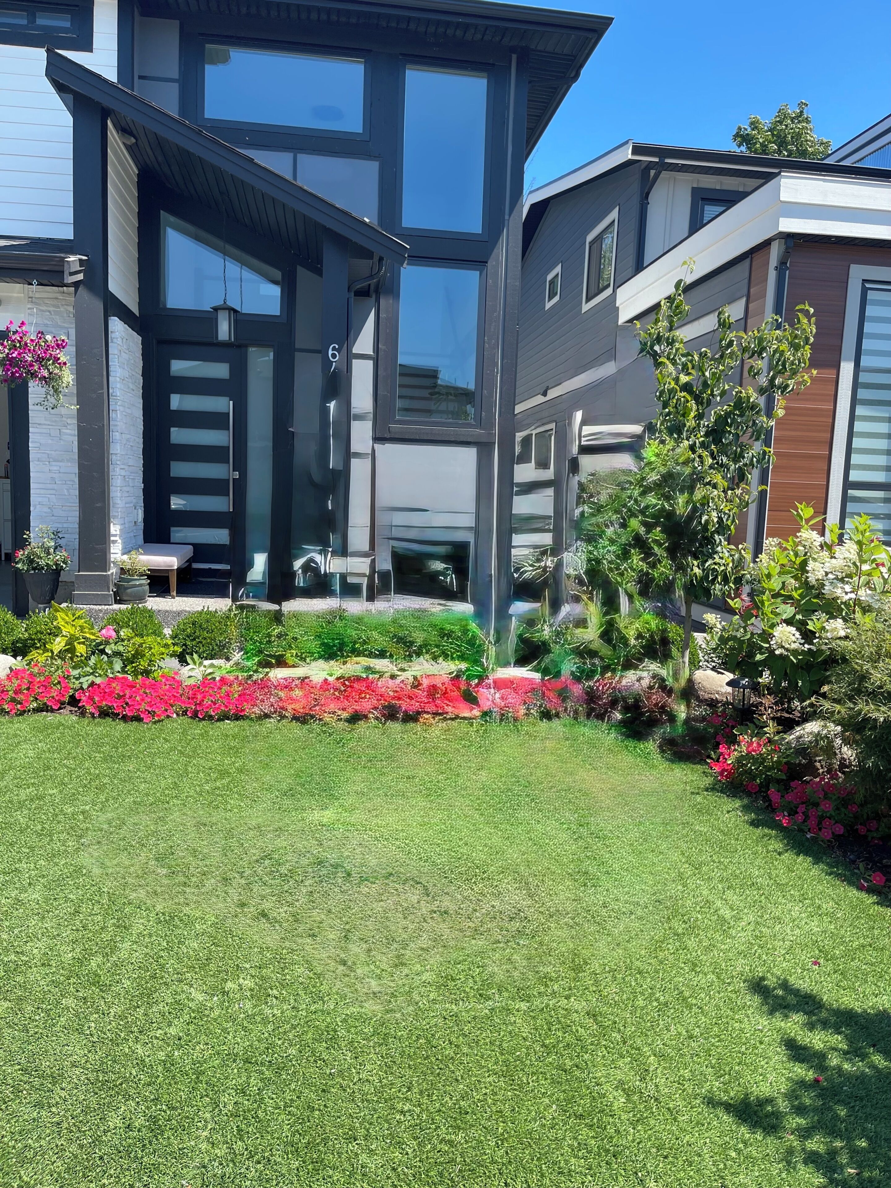 Une maison moderne à deux étages, dotée d’une pelouse bien entretenue et agrémentée de diverses plantes à fleurs.