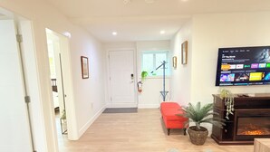 Een moderne woonkamer met een flatscreen televisie aan de wand, een rode bank, een grijze fauteuil en een bijzettafeltje met een plant.