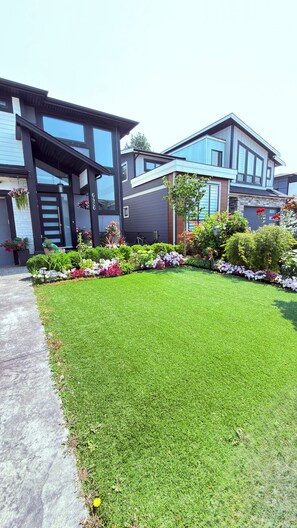 A modern two-story house with a well-maintained lawn and a variety of flowering plants.