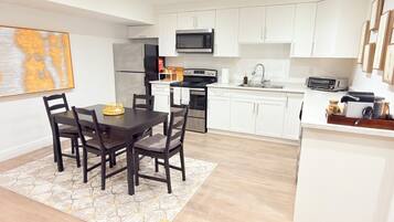 Une cuisine moderne avec des meubles blancs, une table à manger avec des chaises et un four à micro-ondes placé au-dessus de la cuisinière.