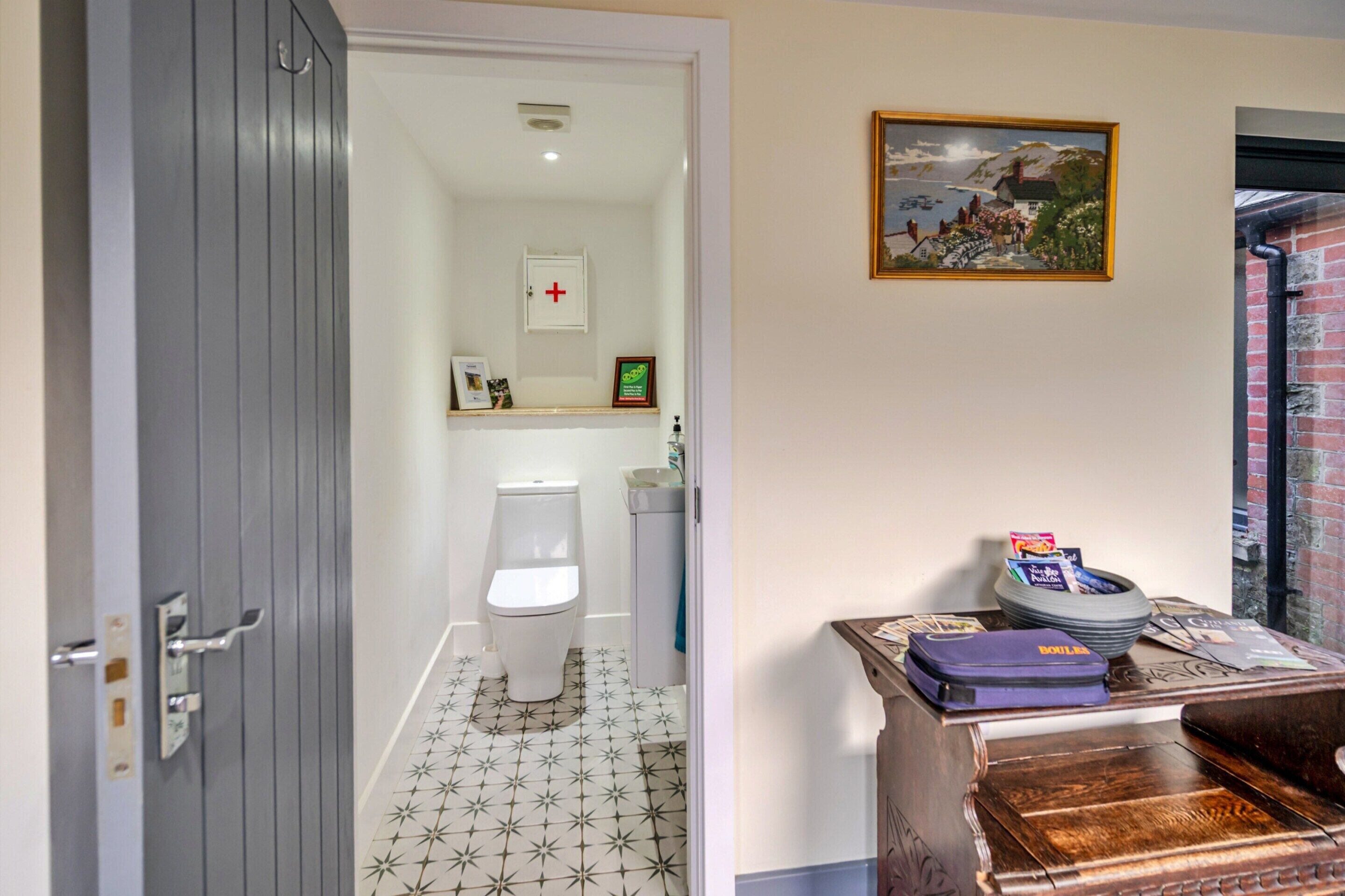 Et badeværelse med toilet, vask og bruser. Der er et indrammet billede på væggen og en lille hylde med toiletartikler.