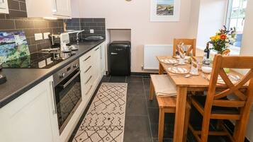 Una cocina funcional con un refrigerador negro, una mesa para dos personas y un tapete estampado en el suelo.