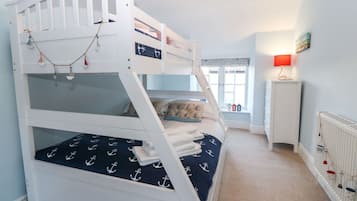 Un llit superposat amb roba de llit de temàtica marina, una finestra amb vistes i un radiador amb decoracions penjades.