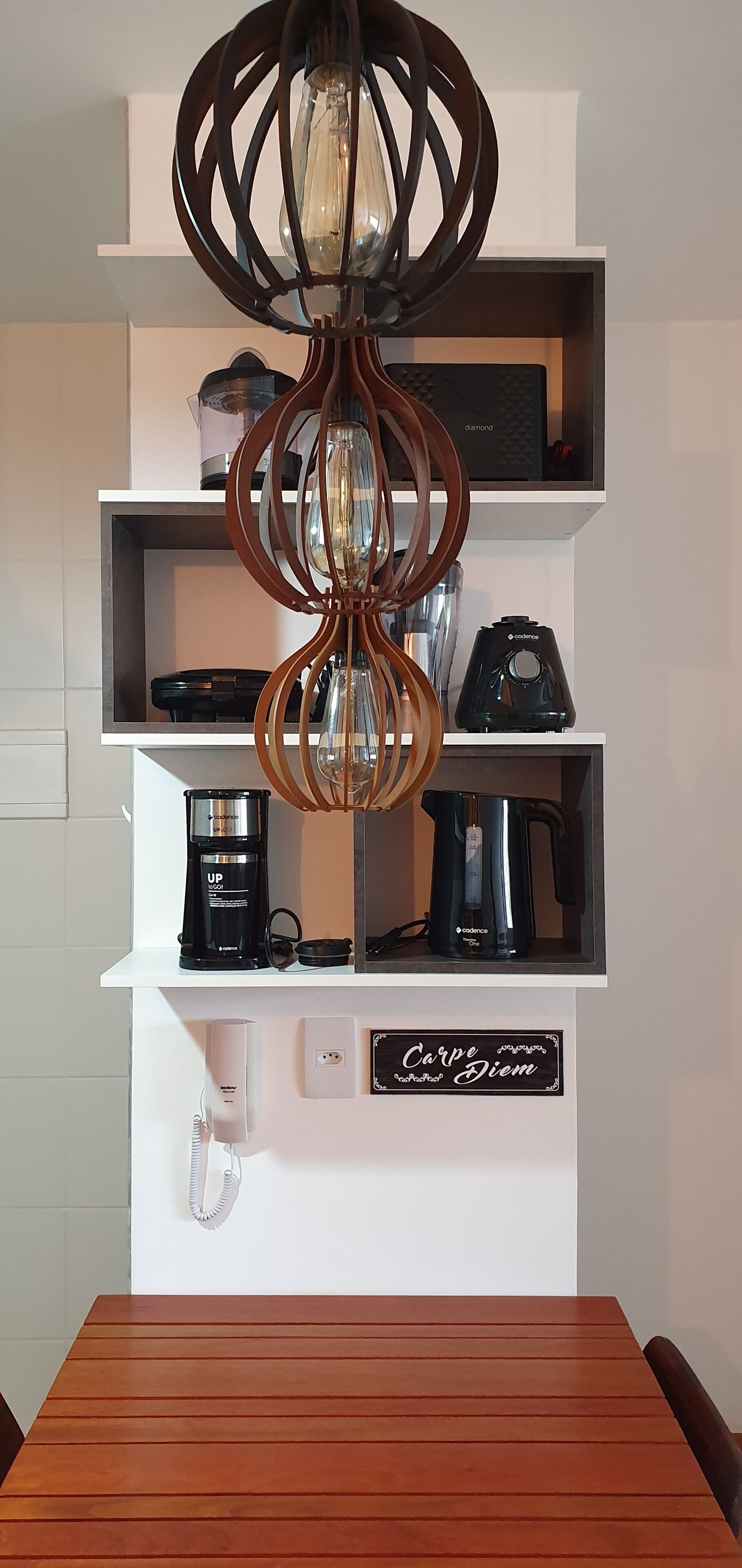 Een moderne keuken met een houten tafel, een koffiezetapparaat, een waterkoker en een aan de muur bevestigd toestel.