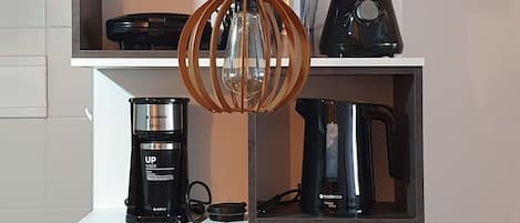 Una cocina moderna con una mesa de madera, una cafetera, un hervidor y un teléfono en la pared.