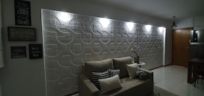 Un salon moderne avec un canapé, des coussins décoratifs, un mur orné de motifs géométriques et une petite table d’appoint sur laquelle est posée une plante.