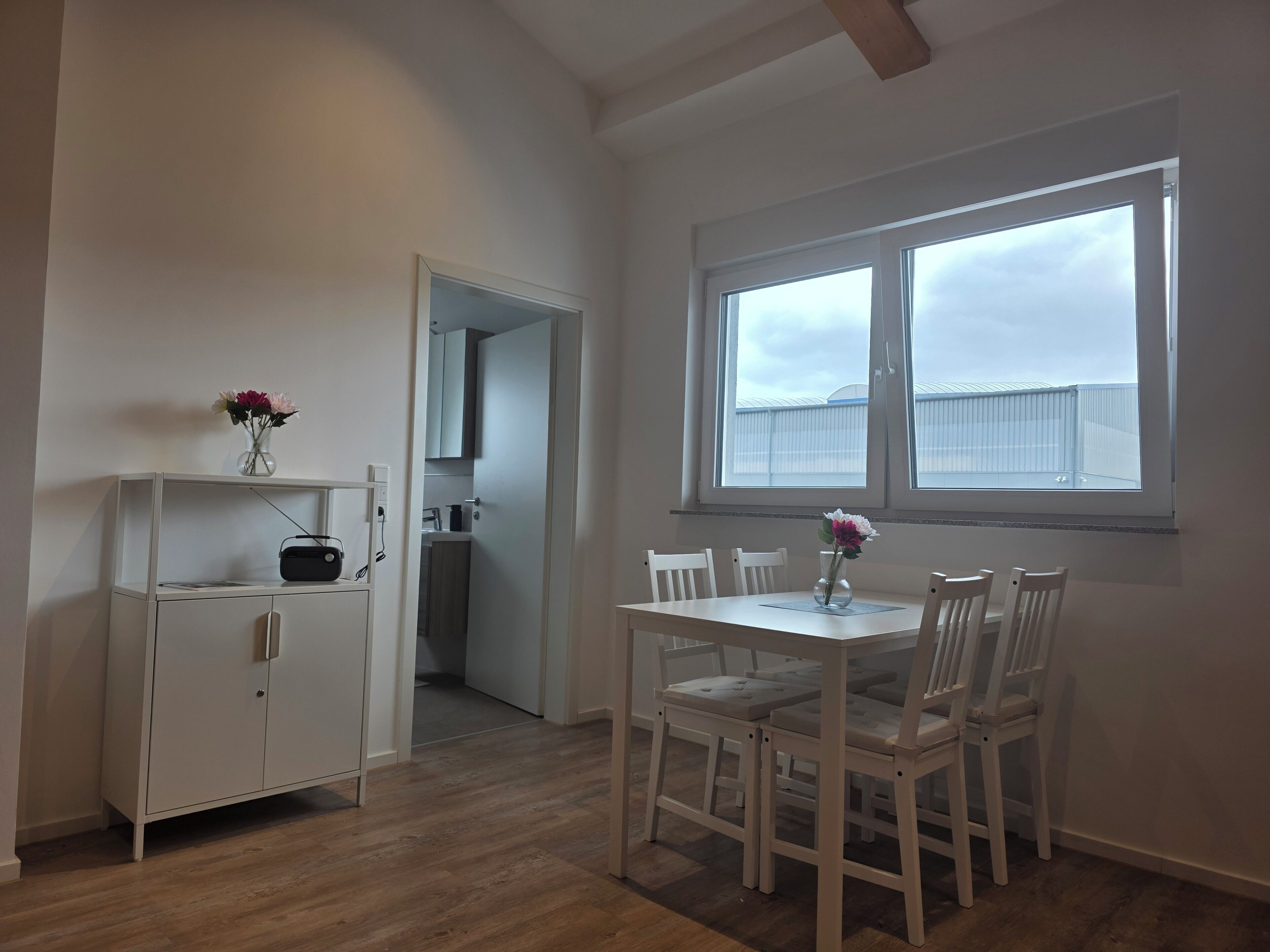 Ein Zimmer mit Esstisch, Stühlen, einem weißen Schrank und einem Fenster mit Blick zum Himmel.