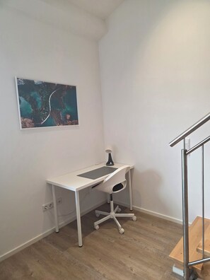 A white desk with a computer, a lamp, and a wall-mounted picture.