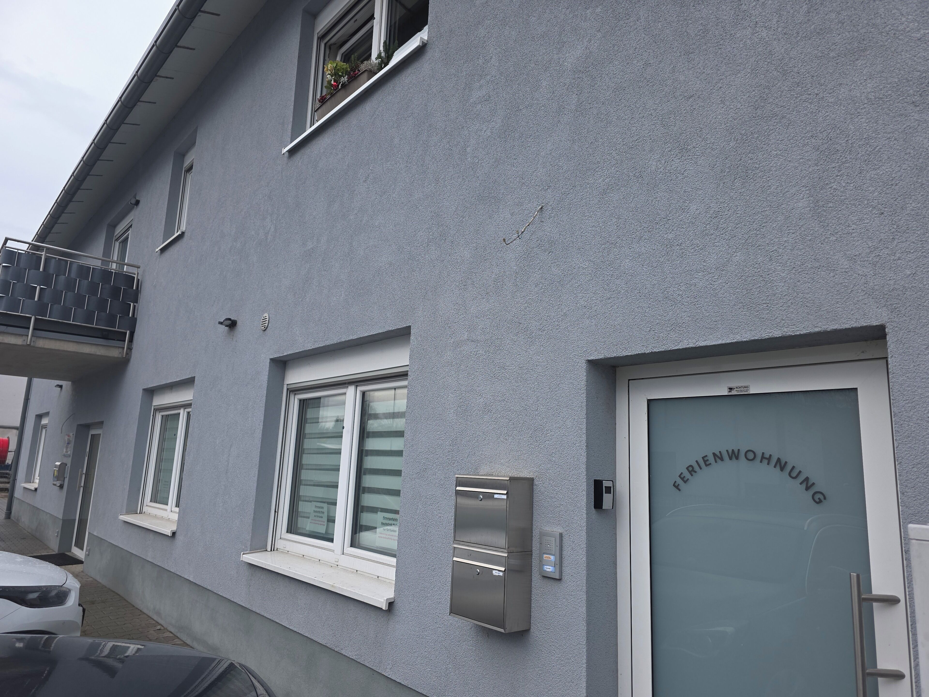 Ein Gebäude mit einer grauen Fassade, einer Tür mit der Aufschrift 'FERRIWOHNUNG' und einem kleinen Fenster mit Rollläden.
