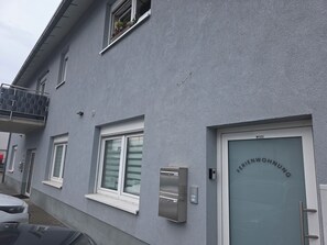 Ein Gebäude mit einer grauen Fassade, einer Tür mit der Aufschrift 'FERRIWOHNUNG' und einem kleinen Fenster mit Rollläden.