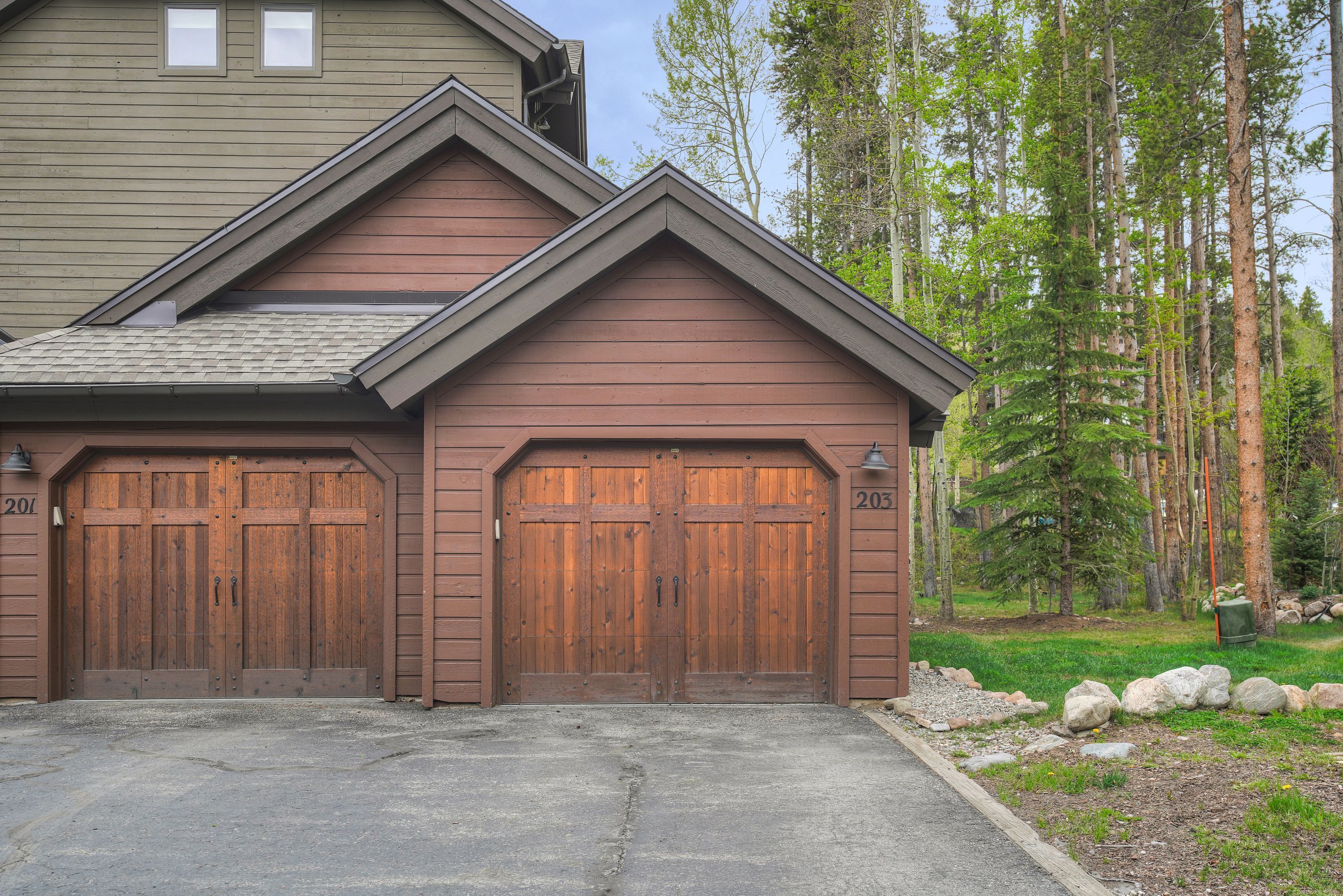 A two-story house with a garage, a driveway, and a forested area in the background.