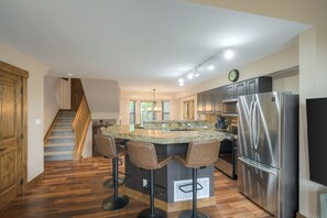 A modern kitchen with a central island, stainless steel appliances, and a wooden staircase.