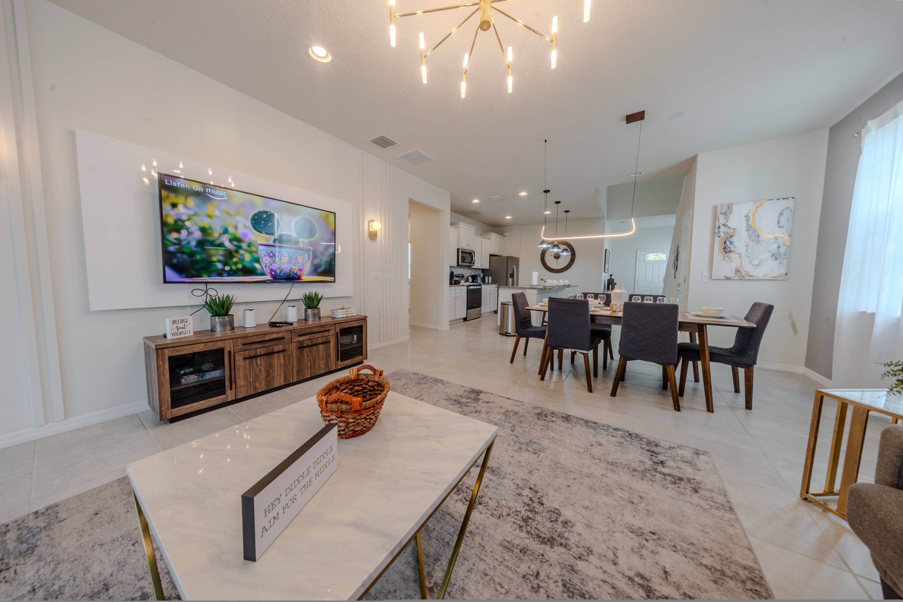 A modern living room with a flat-screen TV, a marble coffee table, and a dining area with a chandelier.